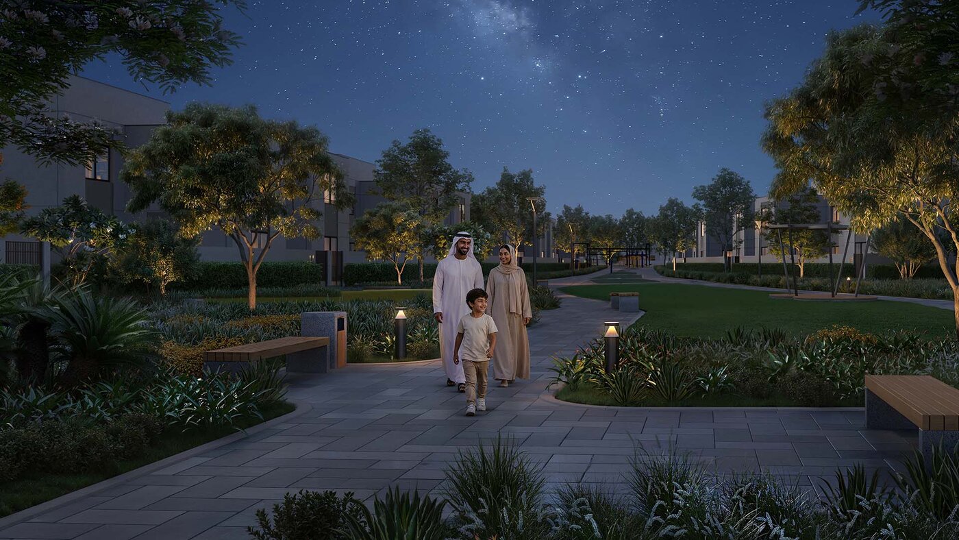 A family walking a lit garden path under a starry sky at Al Ghadeer Parks by Aldar
